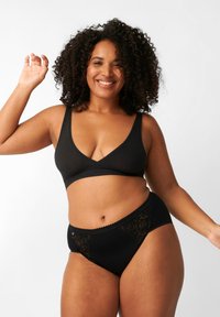 Brasile wireless nera con scollatura profonda e mutandine nere coordinate con dettagli in pizzo e bordi ondulati. Tessuto morbido e elasticizzato.