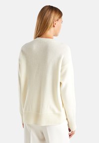 Sweter w kolorze kremowym, wykonany z miękkiego, teksturowanego materiału. Ma prążkowane wykończenie u dołu i na mankietach, luźny krój oraz okrągły dekolt.