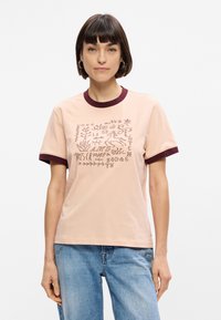 Ροζ βαμβακερή μπλούζα T-shirt με μαρούλι ριμπ κολάρο και μανίκια. Διαθέτει γραφικό σχέδιο με διάφορα σύμβολα και κείμενα εκτυπωμένα μπροστά.