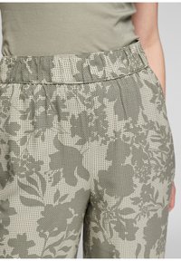 Pantalons à motif floral en vert clair et crème, dotés d'une taille élastique et d'un tissu texturé avec un design perforé.