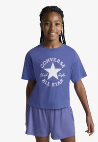 Μωβ βαμβακερό μπλουζάκι με λευκό αστέρι και την επιγραφή «Converse All Star», συνδυασμένο με μωβ σορτς στο ίδιο χρώμα. Casual, κοντομάνικο σχέδιο.