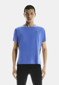 Lekka, niebieska, krótka koszulka sportowa z okrągłym dekoltem, z logo na lewej piersi i teksturowanymi panelami po bokach.