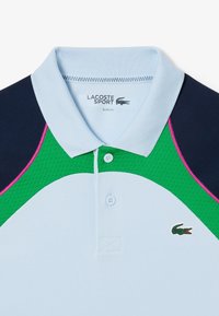 Polo shirt azzurro chiaro con vestibilità slim, caratterizzato da un pannello testurizzato verde, spalle blu scuro, dettagli rosa e un logo sul petto.