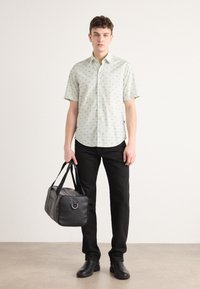 Cămașă scurtă cu mânecă scurtă, de culoare verde deschis, cu un model de frunze, asortată cu pantaloni negri și o geantă de voiaj din piele neagră. Textură netedă și design simplu.
