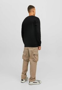 Sudadera negra de mangas largas y puños acanalados, combinada con pantalones cargo beige que cuentan con bolsillos laterales. El modelo es visto desde atrás.