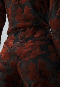 Gros plan sur un tissu noir avec un motif floral en velours rouge foncé en relief sur un vêtement ajusté.