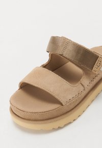 Beige sandaal met twee brede banden, een zachte suede bovenkant, een structuur voetbed en een flexibele rubberen zool met een iets verhoogde rand.