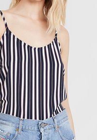 Haut léger sans manches à rayures bleu marine et blanches avec fines bretelles. Le tissu est lisse, présentant des rayures verticales de différentes largeurs.