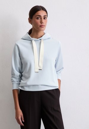 Haut de survêtement bleu clair avec une poche kangourou à l'avant, doté d'un cordon de serrage crème et de poignets côtelés, associé à un pantalon noir.