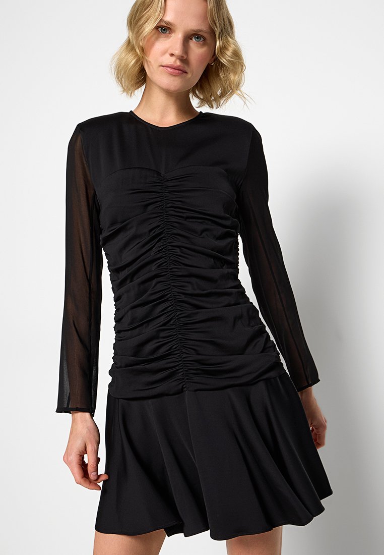 Vestido negro con un cuerpo ajustado que presenta detalles fruncidos y mangas largas transparentes. La falda se abre suavemente por debajo de la cintura, creando una silueta fluida.