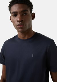 Tmavě modré tričko s krátkým rukávem vyrobené z hladké bavlny, zdobené decentním vystouplým logem 'B' na hrudi. Jednoduchý kulatý výstřih.