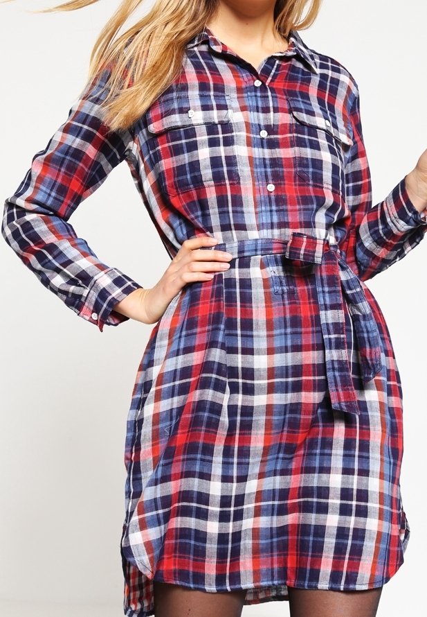 Robe chemise à carreaux rouge, bleu marine et blanc avec manches longues, deux poches poitrine, détail de taille nouée, et ourlet arrondi.