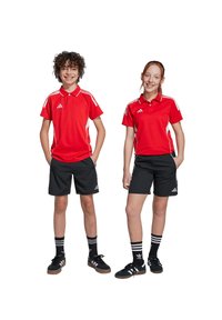 Rode sportieve polo-shirts met witte accenten, gecombineerd met zwarte shorts. Beide dragen zwarte sneakers en gestreepte sokken, wat een sportieve uitstraling creëert.