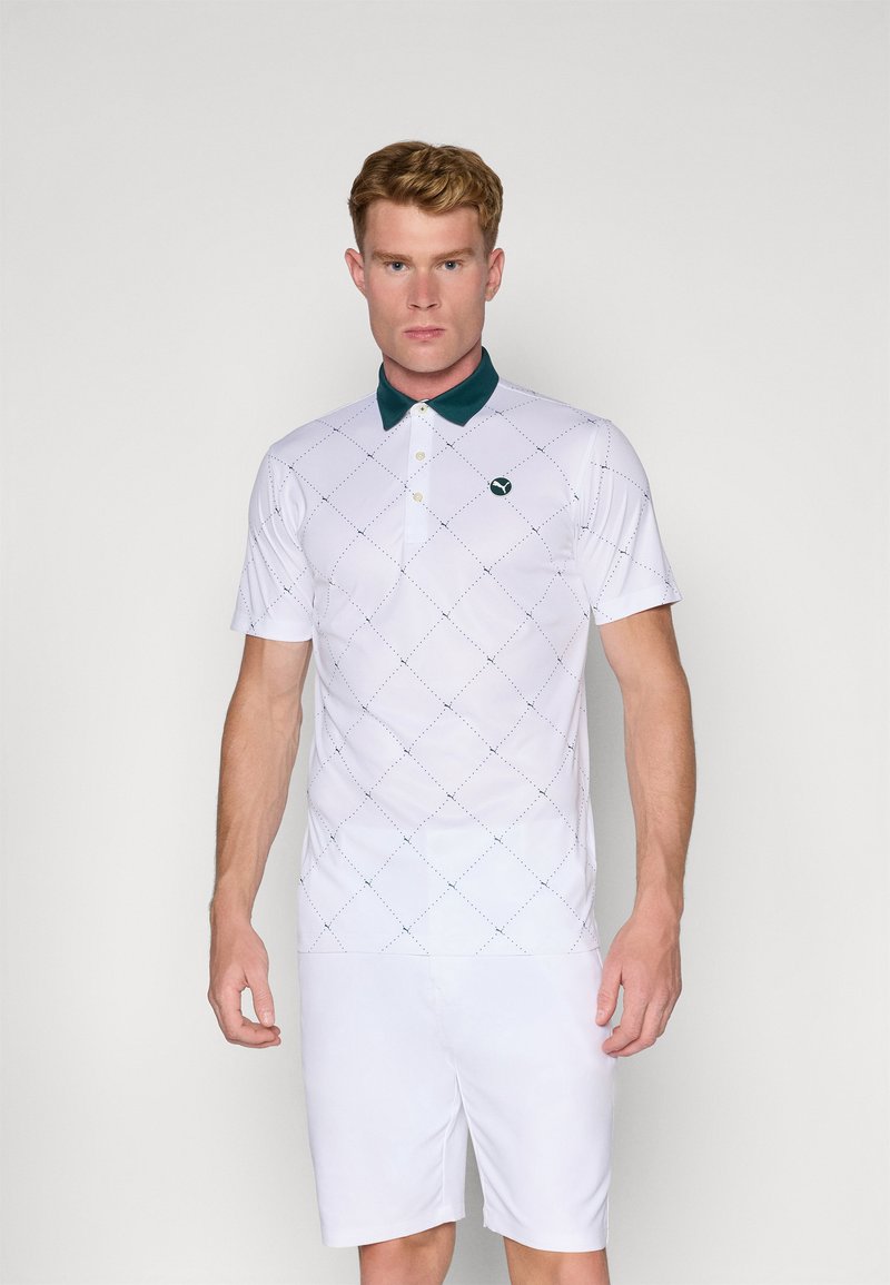 Hvid polo skjorte med korte ærmer og grøn krave, der har et diamantmønster og logo på venstre bryst. Bæres med hvide shorts.