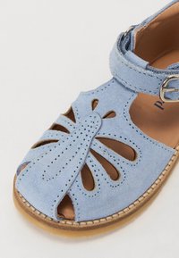 Plave suede sandale s izrezanim uzorcima, podešavanje na gležnju i smešnom potplatu s detaljima šivanja.
