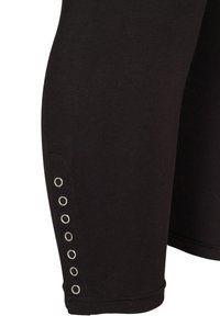 Czarne legginsy uszyte z miękkiego materiału, o dopasowanym kroju, z metalowymi oczkami wzdłuż boków, które dodają detalu i struktury.