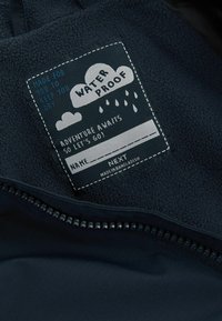 Marineblauwe fleece-voering jack met een waterdichte label, afgebeeld met grafische wolken en regendruppels, witte stiksels en een binnenzak met rits.