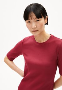 Rode geribde gebreide top met korte mouwen en een ronde halslijn. Soepele textuur en een getailleerde snit, die de rekbaarheid en elasticiteit van de stof benadrukt.