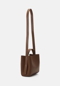 Brun läder tote-väska med en strukturerad form, försedd med en lång rem och ett kort handtag. Slen yta och minimalistisk design.