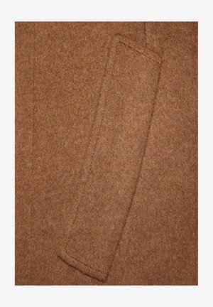 Brązowa wełniana tekstura płaszcza z lewą kieszenią naszywaną o starannym wykończeniu szwów. Materiał wydaje się miękki i gęsty, prezentując gładkie wykończenie.