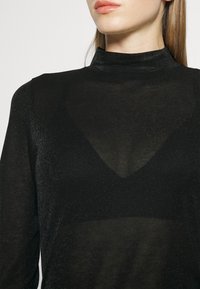 Musthave mustasade, mis on valmistatud pehmest ja läbipaistvast kangast, V-kujuliste detailidega ja delikaatse säraefektiga. Sile viimistlus ning keha külge pigistav disain.