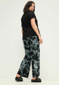 Černé žebrované tričko s krátkým rukávem spárované s volnými kalhotami s černobílým tie-dye vzorem. Modelka má na sobě černé slip-on boty s plochou podrážkou.