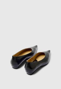 Ballerines noires en cuir à bout pointu avec un talon bas. Les chaussures ont une texture lisse et un design ouvert à l'arrière. Intérieur doublé d'une couleur beige.