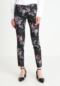 Pantalon noir à motif floral avec des nuances de rose et de gris, coupe slim avec une taille standard, associé à des escarpins noirs.