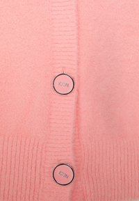 Rosa Strickjacke aus weichem, strukturiertem Material mit Rippendetails und zwei runden Knöpfen, die jeweils mit "ICON" beschriftet sind.