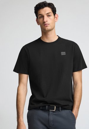 Schwarzes Baumwoll-T-Shirt mit Rundhalsausschnitt, kurzen Ärmeln und einem kleinen, strukturierten Logo-Patch auf der linken Brust. Glattes Material, lässige Passform.