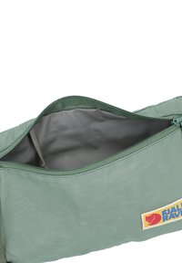 Saco de tecido verde com abertura com fecho, apresentando um forro interno liso e um emblema da Fjällräven em vermelho e azul.