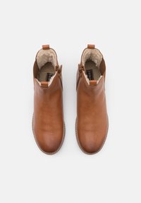 Bottines en cuir marron avec doublure en polaire beige, zips sur le côté et tirettes, présentées en vue de dessus sur fond blanc.