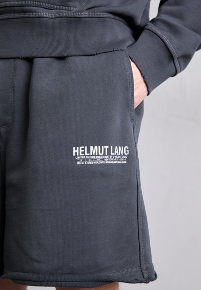 Mørkegrå joggebukser med teksturert stoff, med en lomme foran og hvit trykket logo detaljer på venstre lår. Designet er avslappet.