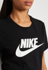 Camiseta de algodón negra con un prominente logo y swoosh blancos de Nike. El cuello es redondo, con una textura suave y mangas cortas.