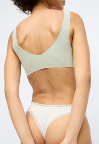 Lichtgroene, naadloze bh met brede bandjes en een diepe rug. Witte slip met kantafwerking. Zachte, gladde stof.