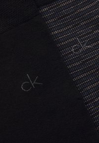 Fekete és tengerészkék mintás zokni, amelynek egyik oldalán textúrált minta található, és egy szürke hímzett "ck" logó díszíti.
