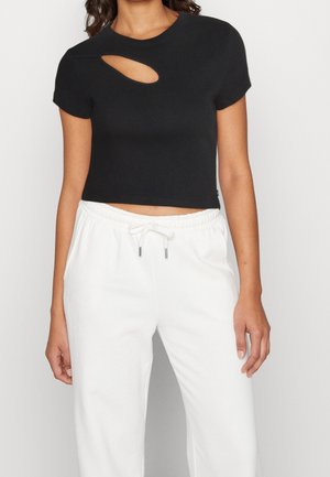 Kobieta ubrana w czarny krótki top z krótkim rękawem z owalnym wycięciem przy dekolcie oraz białe spodnie dresowe ze sznurkiem.