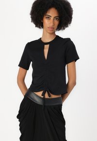 Top negru cu maneci scurte, cu deschidere tip cheie, detalii strânse și un șnur la talie. Fabricat dintr-un material moale și elastic.