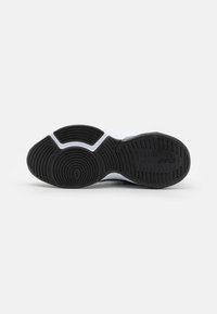 Black rubber shoe sole with textured tread pattern, featuring a white midsole and contrasting grooves for traction and flexibility.