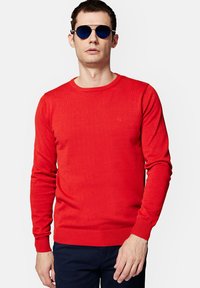 Czerwony sweter z dzianiny, z długimi rękawami i okrągłym dekoltem. Rękawy i dół z prążkowanymi końcówkami. Dyskretne logo na klatce piersiowej. Jednolity kolor, gładka faktura.