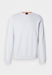Sweat-shirt blanc à manches longues col rond avec poignets et ourlet côtelés, petit logo embossé sur la poitrine et étiquette orange à l'intérieur du col.