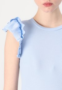 Svetlomodrý rebrovaný top s okrúhlym výstrihom a volánovými rukávmi. Textílie vyzerá hladko a strih je priliehavý.