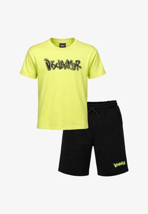 T-shirt gialla a maniche corte con testo graffiti "Disclaimer" e pantaloncini elastici neri con piccolo logo coordinato sulla gamba sinistra.