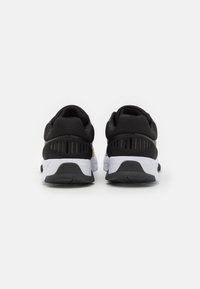 Chaussures de sport noires avec une tige texturée, une semelle blanche et des détails noirs. Présentent des perforations sur les côtés pour la ventilation.