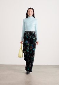 Pulover din bumbac bleu deschis cu guler înalt, pantaloni negri largi cu imprimeu floral colorat, geantă galbenă și cizme negre. Material neted, design lejer.
