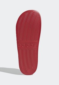 Röd gummisula med ett fiskbensmönster och präglad "adidas"-logotyp. Slät yta med rundade kanter och subtila detaljer.