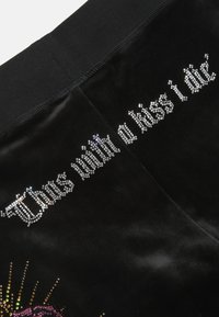 Crna baršunasta tkanina sa kristalnim ukrasima i natpisom "Ovim umirem s poljupcem" te šarenim grafičkim dizajnom ispod.