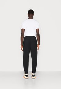 Pantaloni sportivi neri con una cintura elastica, design affusolato, indossati con una maglietta bianca e sneakers multicolori.