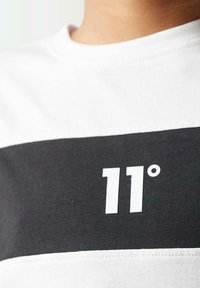 Camiseta de manga corta en algodón blanco y negro, con un destacado gráfico blanco "11°" en el centro. Tejido texturizado con bloques de color sólido.