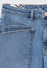 Jeans in denim azzurro chiaro con vita alta, dotati di doppie tasche frontali e cuciture a contrasto lungo le cuciture.